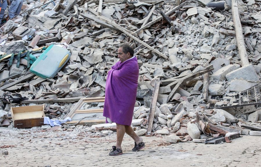 epa05508231 A man covered in a blanket walks in front of the rubble of collapsed buildings in Amatrice, central Italy, 24 August 2016, following a 6.2 magnitude earthquake, according to the United States Geological Survey (USGS), that struck at around 3:30 am local time (1:30 am GMT). The quake was felt across a broad section of central Italy, including the capital Rome where people in homes in the historic center felt a long swaying followed by aftershocks. According to reports at least 21 people died in the quake, 11 in Lazio and 10 in Marche regions. EPA/MASSIMO PERCOSSI