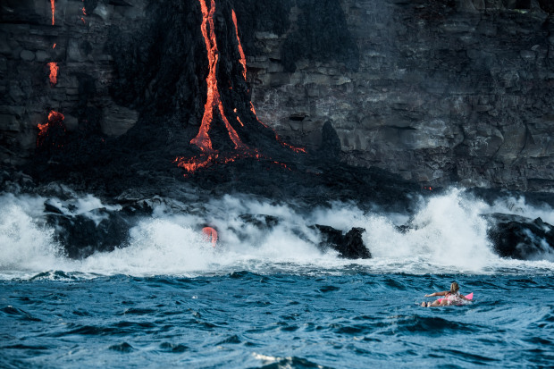 PIC BY PERRIN JAMES / CATERS NEWS - (PICTURED: Alison Teal paddles out to Kilauea volcano in Hawaii as it eruopts into the ocean) - Professional adventurer Alison Teal has become the first woman to paddle out into lava during a volcanic eruption into the sea. Amazing shots of the extreme surf session shows the daredevil riding her pink surfboard up to the base of Kilauea Volcano. Photographer Perrin James snapped the brave explorer within feet of the lava as it flows into the ocean. Its the first the volcano in the Big Island of Hawaii has erupted since 2011. SEE CATERS COPY