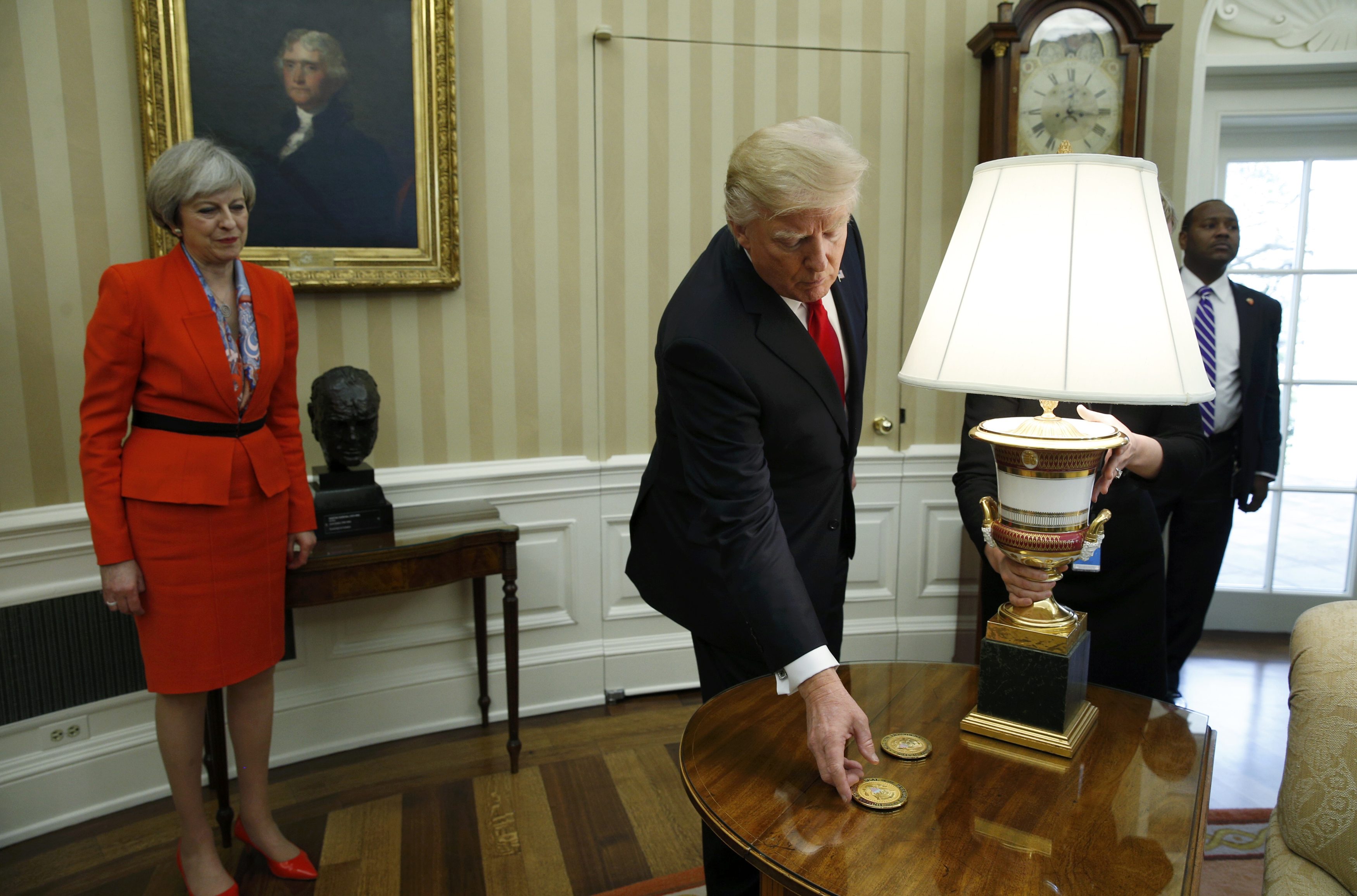 U.S. President Donald Trump reaches for a gift to present to British Prime Minister Theresa May in the White House Oval Office in Washington, U.S., January 27, 2017.  REUTERS/Kevin Lamarque