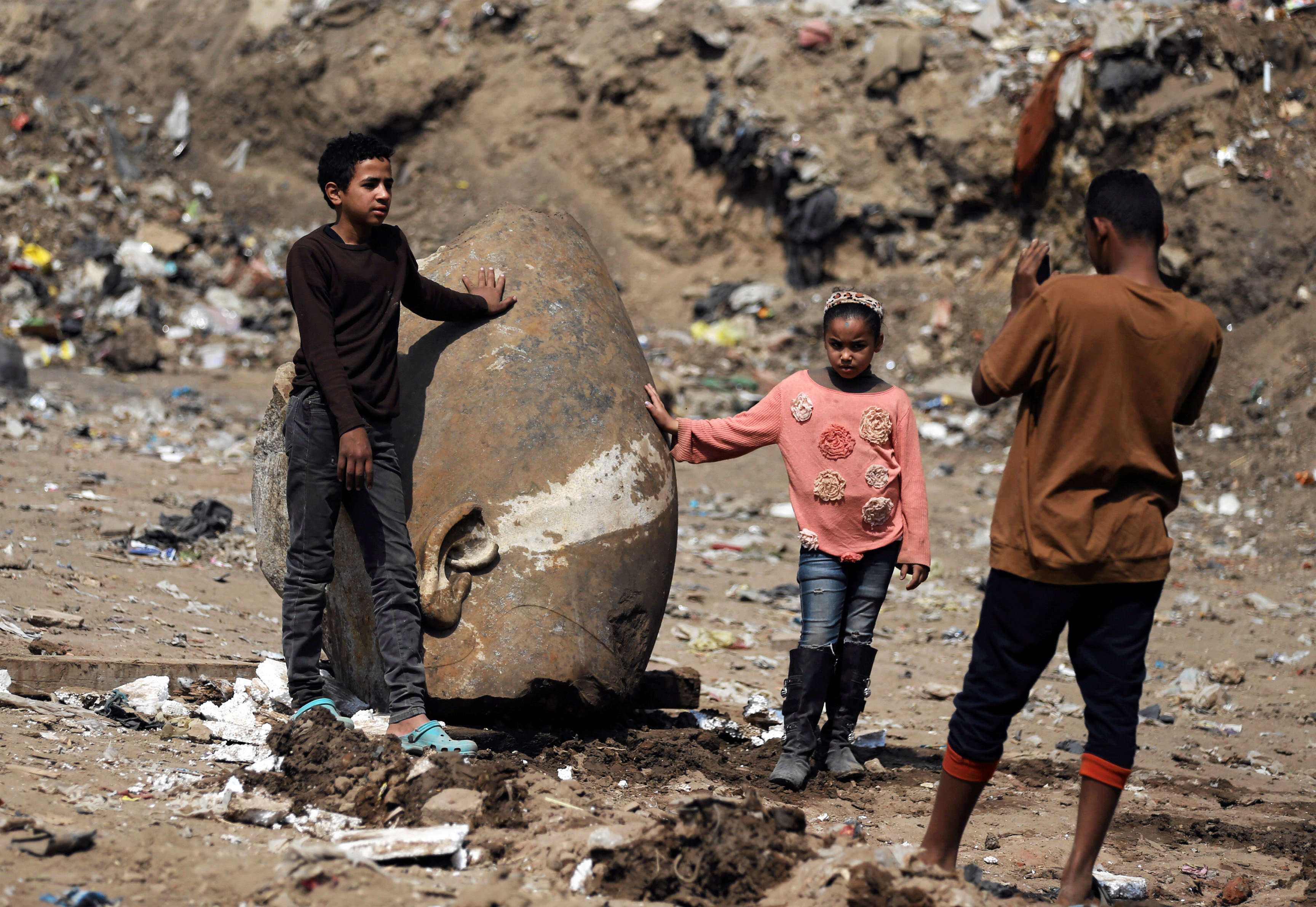 Matariya residents rest against what appears to be the head of an unearthed statue that workers say depicts Pharaoh Ramses II, in Cairo