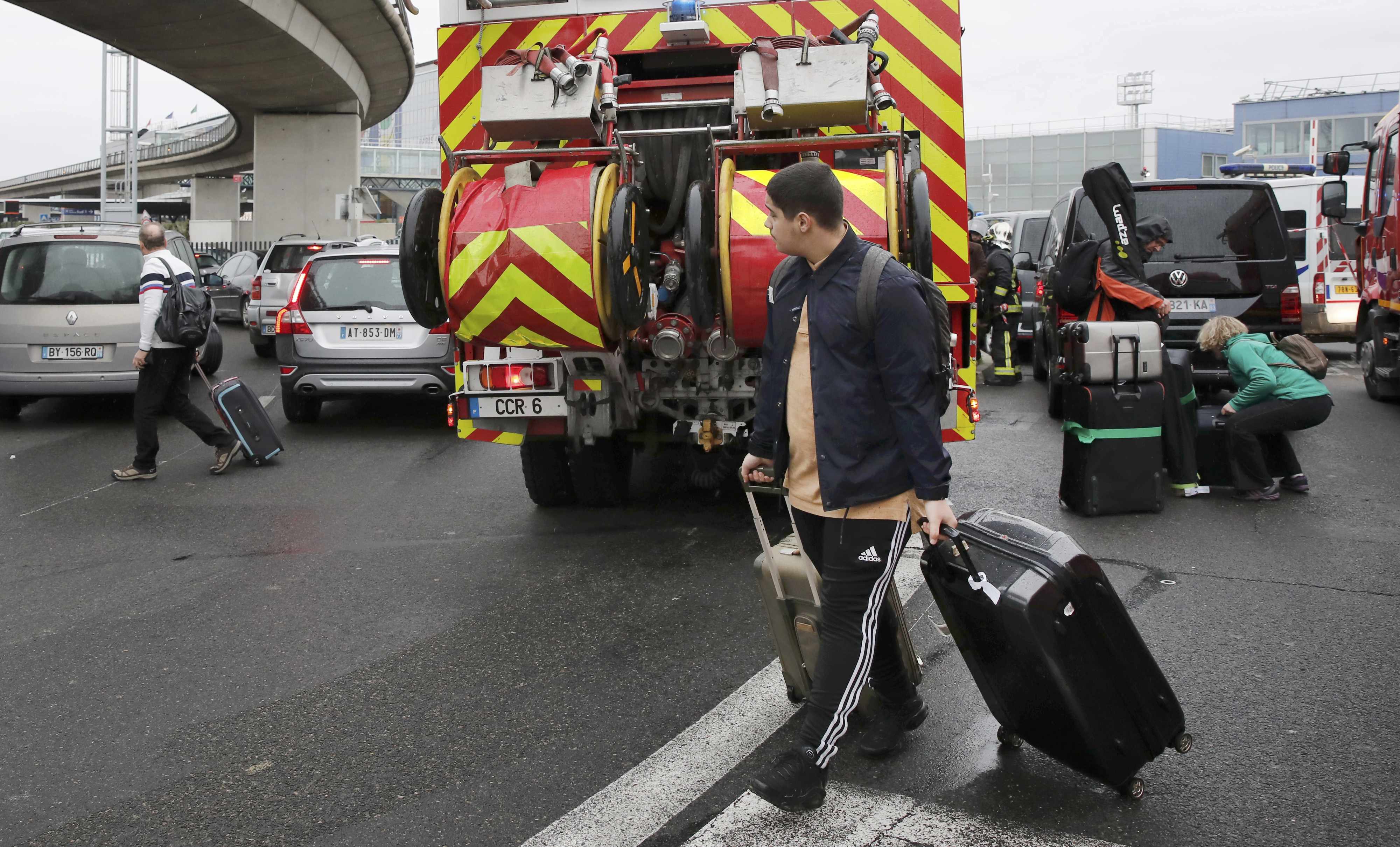 Passengers pass emergency vehicles at Orly airport southern terminal after shooting incident near Paris
