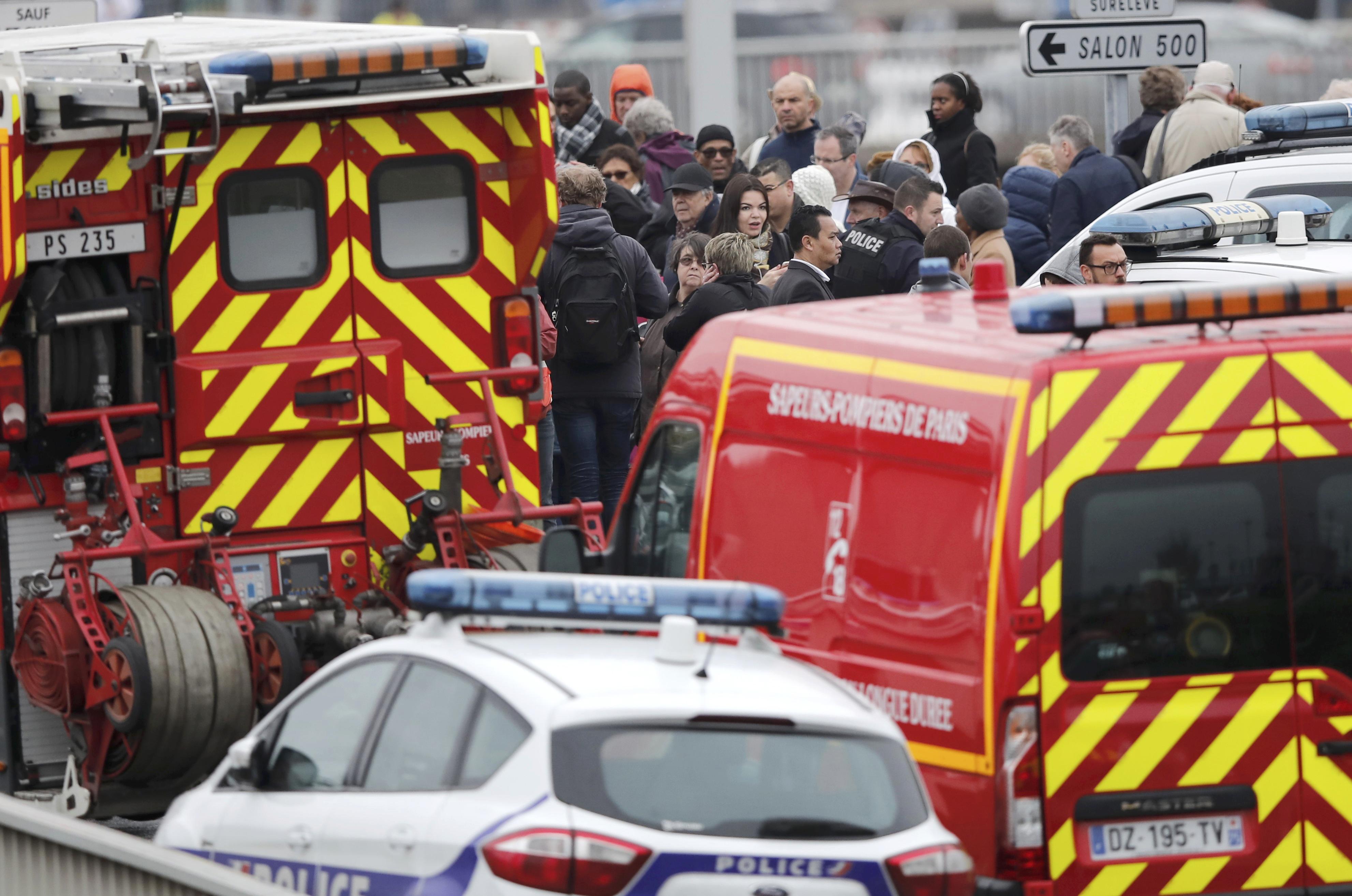 Passengers wait amongst emergency vehicles at Orly airport southern terminal after shooting incident near Paris