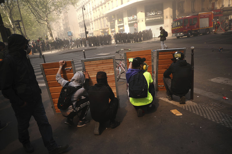 Protestos take shelter behind wooden panels during a yellow vest demonstration in Paris, Saturday, April 20, 2019. French yellow vest protesters are marching anew to remind the government that rebuilding the fire-ravaged Notre Dame Cathedral isn't the only problem the nation needs to solve. (AP Photo/Francisco Seco)