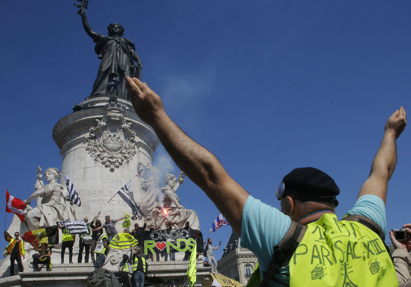 A protestor puts his arms in the air at the Place de Republique during a yellow vest demonstration in Paris, Saturday, April 20, 2019. French yellow vest protesters are marching anew to remind the government that rebuilding the fire-ravaged Notre Dame Cathedral isn't the only problem the nation needs to solve. (AP Photo/Michel Euler)