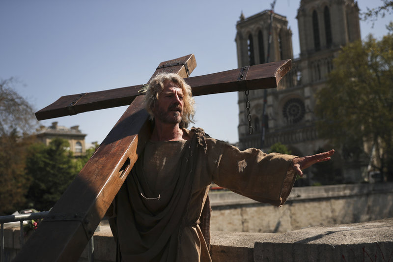 A man carries a wooden cross outside the Notre Dame Cathedral as part of a demonstration in Paris, Saturday, April 20, 2019. French yellow vest protesters are marching anew to remind the government that rebuilding the fire-ravaged Notre Dame Cathedral isn't the only problem the nation needs to solve. (AP Photo/Francisco Seco)