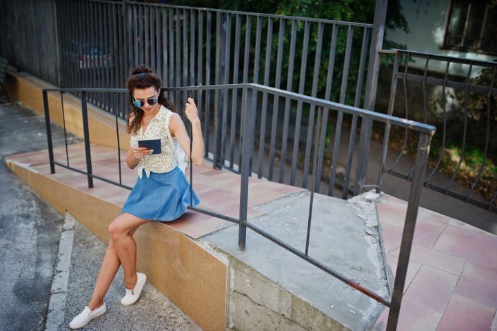 Curly stylish girl wear on blue jeans skirt, blouse with tablet on hands.