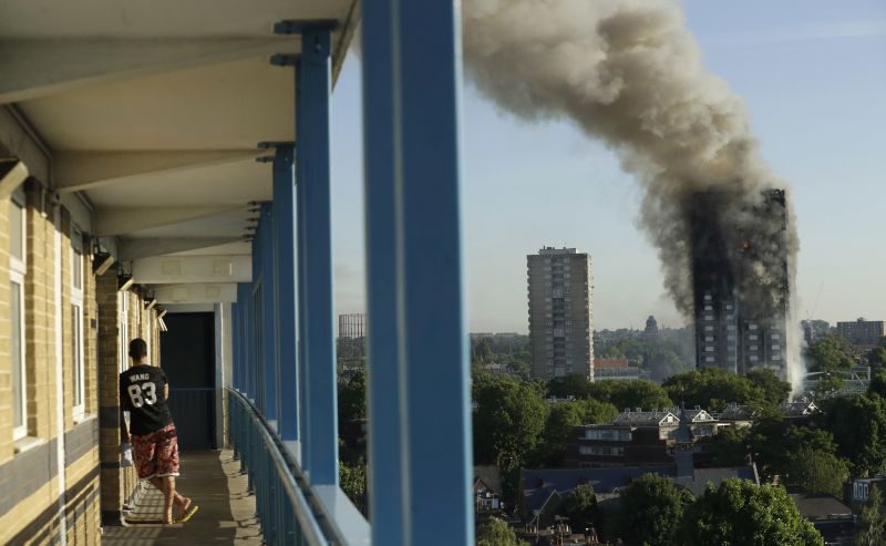 CORRECTS FLOOR NUMBER - A resident in a nearby building watches smoke rise from a building on fire in London, Wednesday, June 14, 2017. A massive fire raced through the 24-story high-rise apartment building in west London early Wednesday, sending many people to hospitals, emergency officials said. (AP Photo/Matt Dunham)