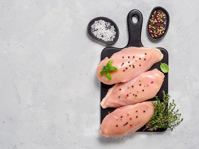 Raw chicken breast with fresh basil and thyme on black cuttingboard. Raw chicken fillet on gray cement background. Copy space. Top view or flat lay.