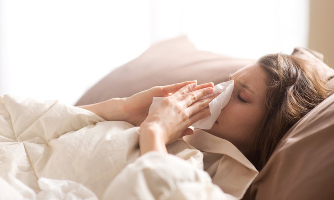 sick woman blowing her nose while in bed