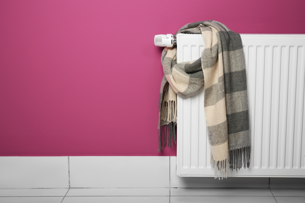 Warm scarf drying on heating radiator on pink wall background