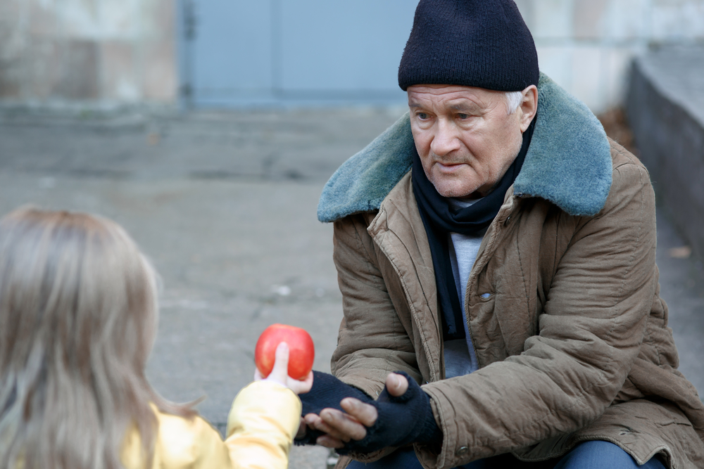 Getting food. Kind little girl gives apple to a homeless person.