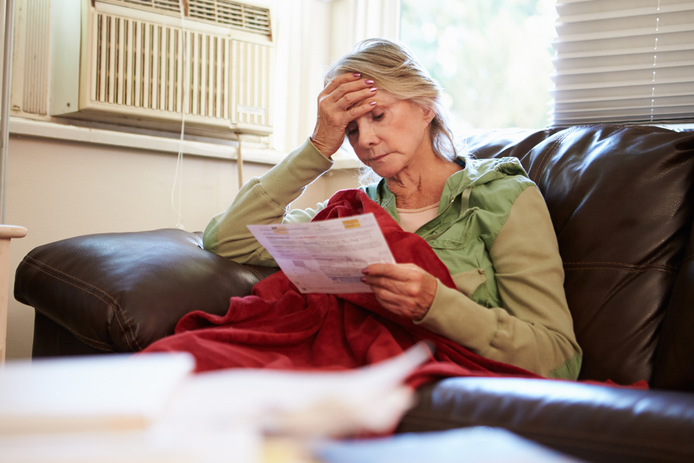 Worried Senior Woman Sitting On Sofa Looking At Bills
