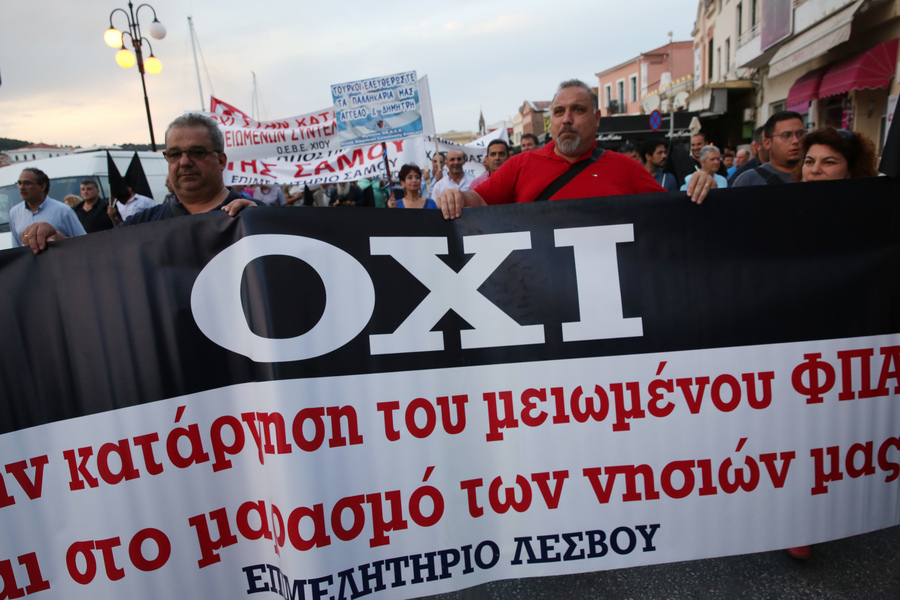 Διαδηλωτές κρατώντας πανό και μαύρες σημαίες σε συγκέντρωση διαμαρτυρίας έξω από το Αίθριο της Γενικής Γραμματείας Αιγαίου, όπου θα μιλήσει ο πρωθυπουργός Αλέξης Τσίπρας στο 14ο Περιφερειακό Συνέδριο για την Παραγωγική Ανασυγκρότηση, στη Μυτιλήνη, την Πέμπτη 3 Μαΐου 2018. Με κινητοποιήσεις, απεργίες και κλειστά καταστήματα αντιδρούν κάτοικοι και φορείς της Λέσβου στην επίσκεψη του πρωθυπουργού Αλέξη Τσίπρα για να συμμετάσχει στο 14ο Αναπτυξιακό Συνέδριο Βορείου Αιγαίου. Πάγιο αίτημα των κατοίκων και των φορέων είναι η άμεση αποσυμφόρηση από τον μεγάλο αριθμό προσφύγων και μεταναστών, αλλά και η διατήρηση των μειωμένων συντελεστών ΦΠΑ. ΑΠΕ ΜΠΕ/ΑΠΕ ΜΠΕ/ΟΡΕΣΤΗΣ ΠΑΝΑΓΙΩΤΟΥ