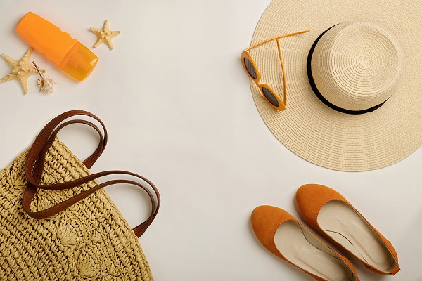 Fashion accessories for the beach - hat, ballet shoes, orange glasses and sunscreen on a white background. Selective focus.