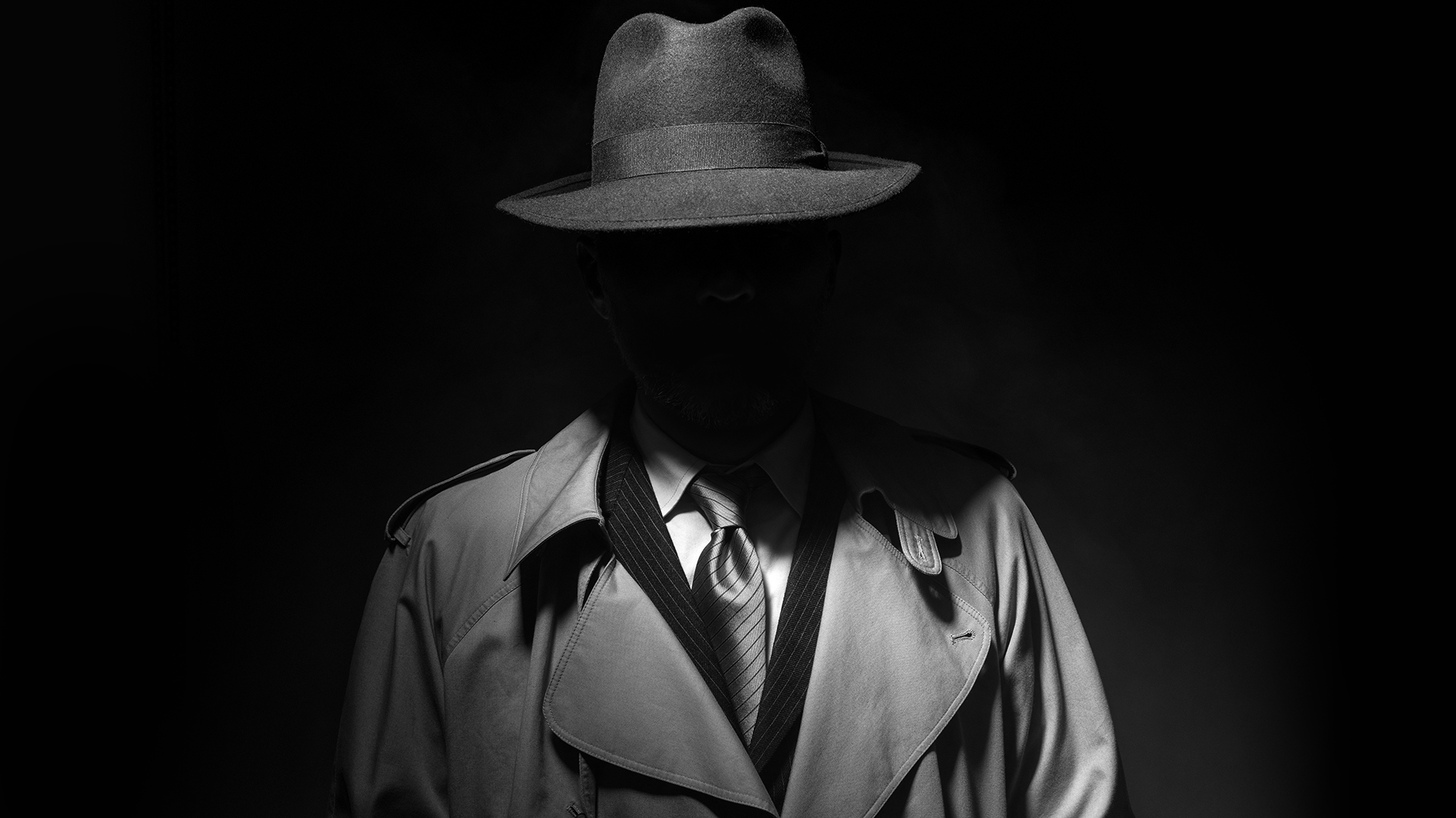 Man posing in the dark with a fedora hat and a trench coat, 1950s noir film style character