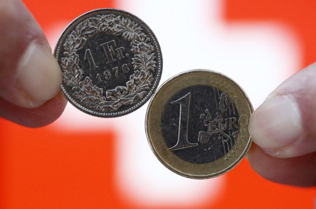 A one Swiss franc coin (L) and a one Euro coin are seen in front of a Swiss flag in this illustration picture in Bern January 18, 2015. German bond yields hit record lows on Friday while fears about Greek banks sent the country's borrowing costs spiralling - signs of the fallout from the Swiss National Bank's shock decision to scrap its currency cap. A surge in the Swiss franc after the SNB abandoned its 1.20 euro limit on Thursday saw investors flee equities and other risky assets, parking money instead in top-rated bonds. REUTERS/Thomas Hodel (SWITZERLAND - Tags: BUSINESS POLITICS)