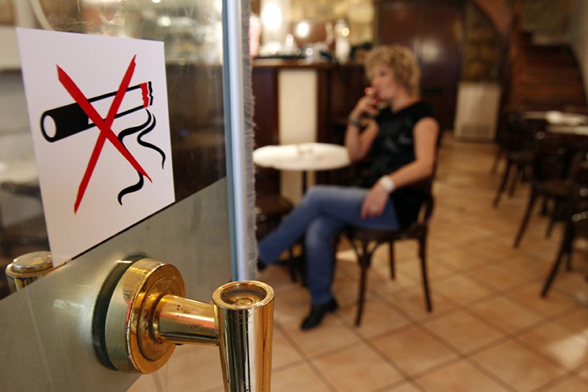 A woman smokes a cigarette behind a smoking ban sign in a restaurant-cafe in central Athens October 18, 2010. Businesses around Greece have decided to violate a smoking ban and have placed ashtrays back on tables and allow customers to smoke inside, despite the law and heavy fines, saying an economic crisis and smoking ban simultaneously is killing business. REUTERS/John Kolesidis (Greece - Tags: POLITICS SOCIETY)