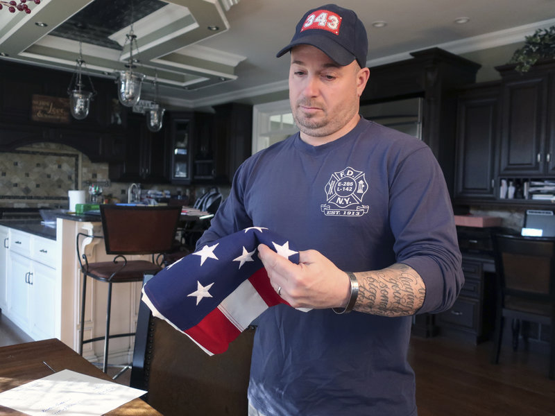 In this January 14, 2019 photo retired firefighter Lt. Michael O'Connell looks at an American flag at his home in Westbury, New York. A Memorial Glade will soon open at the 9/11 Memorial to honor first responders who are sick or who have died from exposure to toxins at the World Trade Center after the 9/11 attacks. O'Connell suffers from sarcoidosis, an inflammatory disease, from his rescue and recovery work after the 9/11 terror attacks. (AP Photo/Ted Shaffrey)