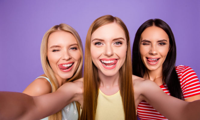 Self portrait of funky cool girls gesturing tongue out winking with one eye enjoying weekend together isolated on bright violet background. Rest relax leisure concept