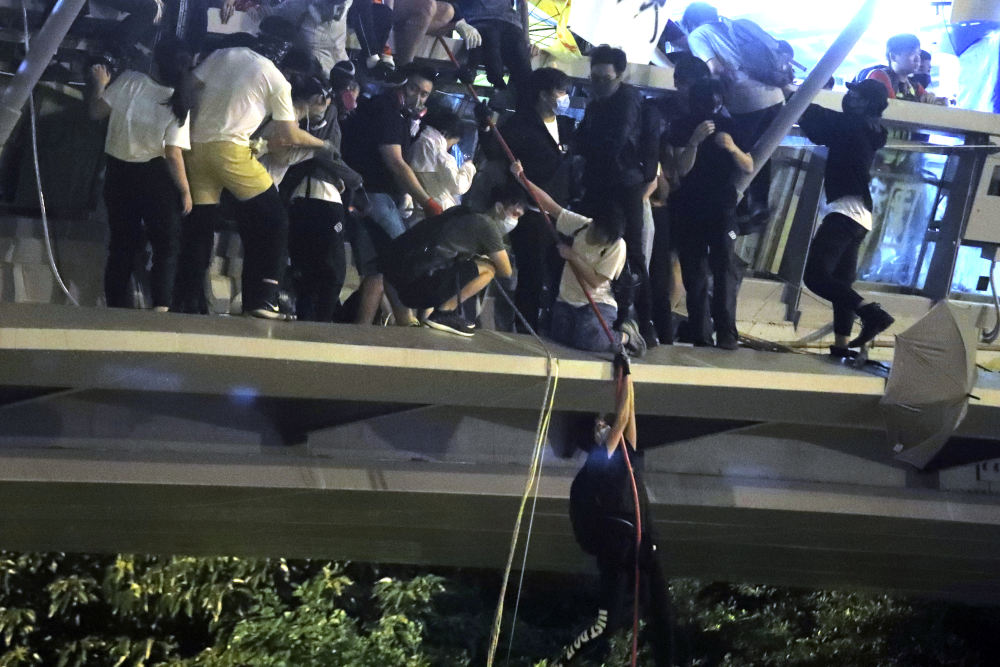 Protestors use a rope to lower themselves from a pedestrian bridge to waiting motorbikes in order to escape from Hong Kong Polytechnic University and the police in Hong Kong, Monday, Nov. 18, 2019. As night fell in Hong Kong, police tightened a siege Monday at a university campus as hundreds of anti-government protesters trapped inside sought to escape. (AP Photo/Kin Cheung)