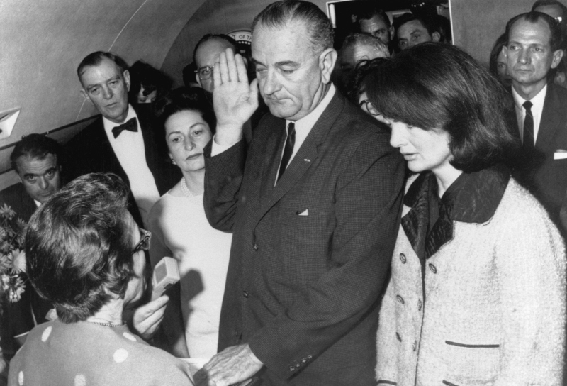 Vice President Lyndon B. Johnson is sworn in to the office of the Presidency aboard Air Force One in Dallas, Texas, hours after the assassination of President John F. Kennedy. Johnson is flanked by wife, Lady Bird Johnson (L), and First Lady Jacqueline Kennedy during the ceremony, which is being administered by U.S. District Judge Sarah Hughes. At farthest left in the background is Jack Valenti. (Photo by © Bettmann/CORBIS/Bettmann Archive)