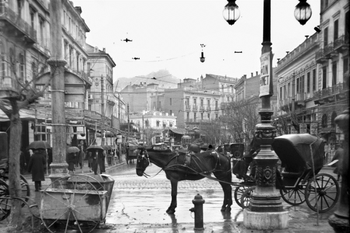 Φωτογραφία αρχείου που δόθηκε σήμερα στη δημοσιότητα και εικονίζει μόνιππα αμάξια, αυτοκίνητα και πεζοί με ομπρέλες να περπατούν μια βροχερή μέρα στην ΑΘήνα του 1927,  στην οδό Πανεπιστημίου από την πλατεία Ομονοίας.  Παρασκευή 25 Ιανουαρίου 2013. Με φωτογραφικό υλικό από τη Συλλογή Πέτρου Πουλίδη, κυριότητας του Αρχείου της ΕΡΤ, η Δημόσια Ραδιοτηλεόραση συμμετέχει στην πολιτιστική δράση «Μια φωτογραφία για την Πατησίων», που διοργανώνεται μέχρι και τις 19 Φεβρουαρίου από το Αθηναϊκό Καλλιτεχνικό Δίκτυο, τον Οργανισμό Πολιτισμού, Αθλητισμού και Νεολαίας του Δήμου Αθηναίων (ΟΠΑΝΔΑ) και  τον Εμπορικό Σύλλογο Αθηνών. Στο φωτογραφικό υλικό του Αρχείου της ΕΡΤ, που εκτίθεται στις βιτρίνες κτιρίου επί της Πατησίων 214, αποτυπώνονται εικόνες της περιοχής από την καθημερινή ζωή των Αθηναίων στις τρεις πρώτες δεκαετίες  του 20ου αιώνα. ΑΠΕ-ΜΠΕ/ΙΣΤΟΡΙΚΟ ΑΡΧΕΙΟ ΕΡΤ/ΣΥΛΛΟΓΗ ΠΕΤΡΟΥ ΠΟΥΛΙΔΗ
