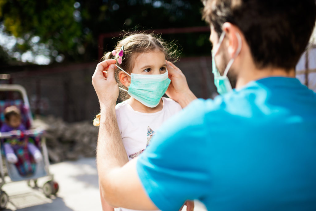 Single father applying pollution mask to his daughter. They are outside.