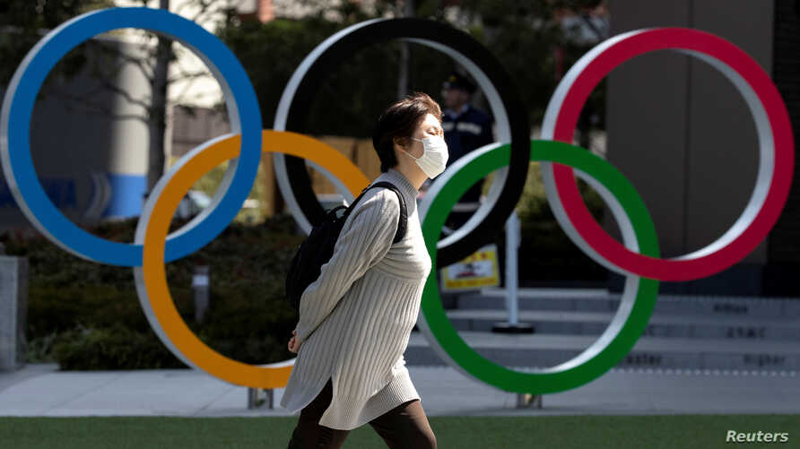 FILE PHOTO: A woman wearing a protective face mask, following an outbreak of the coronavirus disease (COVID-19), walks past the Olympic rings in front of the Japan Olympics Museum in Tokyo, Japan March 13, 2020. REUTERS/Athit Perawongmetha/File Photo