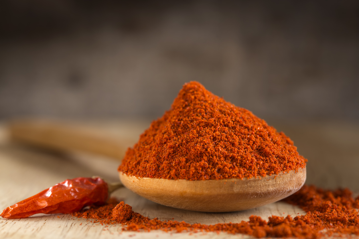 Spoon filled with red hot paprika powder and red hot chili pepper over wooden background