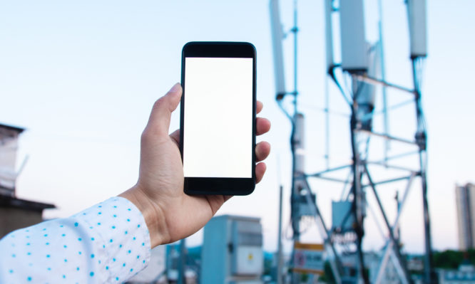 Man holding mobile phone with 5G communications tower background