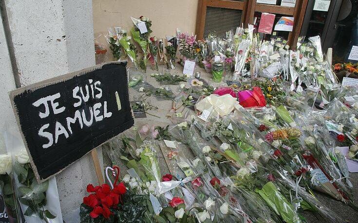 A poster reading "I am Samuel" and flowers lay outside the school where slain history teacher Samuel Paty was working, Saturday, Oct. 17, 2020 in Conflans-Sainte-Honorine, northwest of Paris. French President Emmanuel Macron denounced what he called an "Islamist terrorist attack" against a history teacher decapitated in a Paris suburb Friday, urging the nation to stand united against extremism. The teacher had discussed caricatures of Islam's Prophet Muhammad with his class, authorities said. The suspected attacker was shot to death by police after Friday's beheading. (AP Photo/Michel Euler)