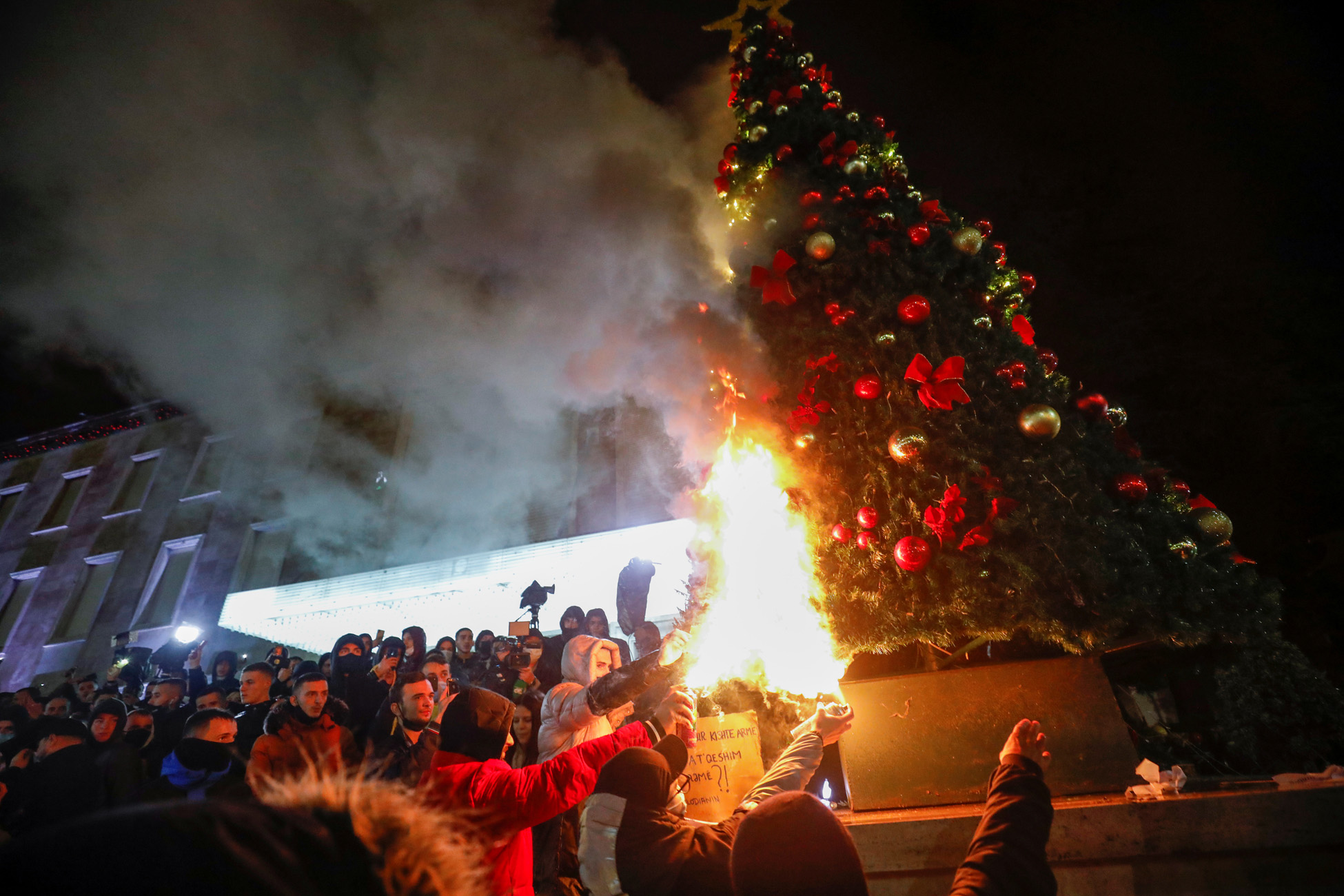 Demonstrators set fire to a Christmas tree in front of the prime minister's office during a protest in reaction to the death of Klodian Rasha, after he was shot dead during the country's overnight curfew, in Tirana, Albania, December 9, 2020. REUTERS/Florion Goga