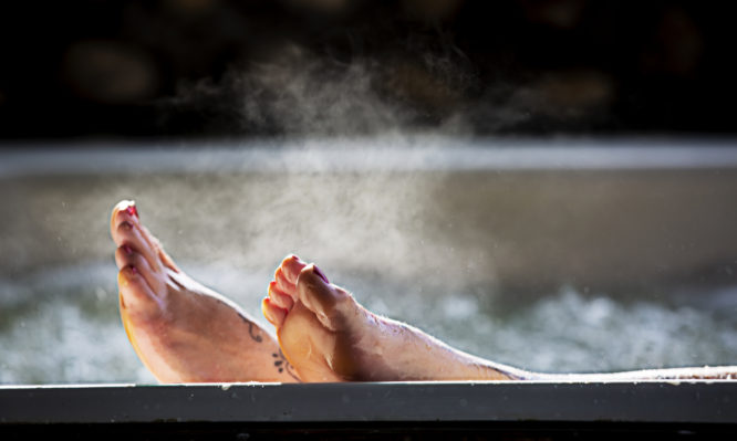 Woman holds her feet up while in a hot tub with steam