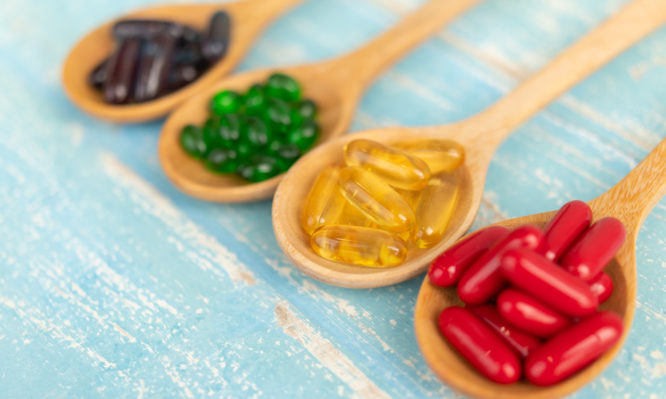 Close-up of colorful soft gelatin capsule supplements in a wooden spoon on a blue background Vintage.