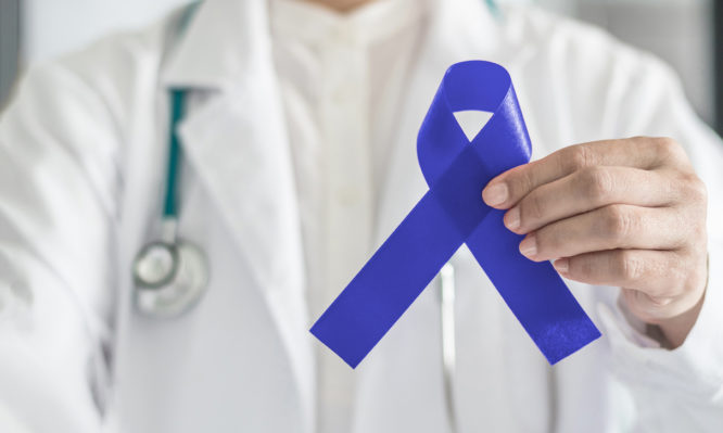 Dark blue ribbon for colon - colorectal cancer awareness on medical doctor's hand support