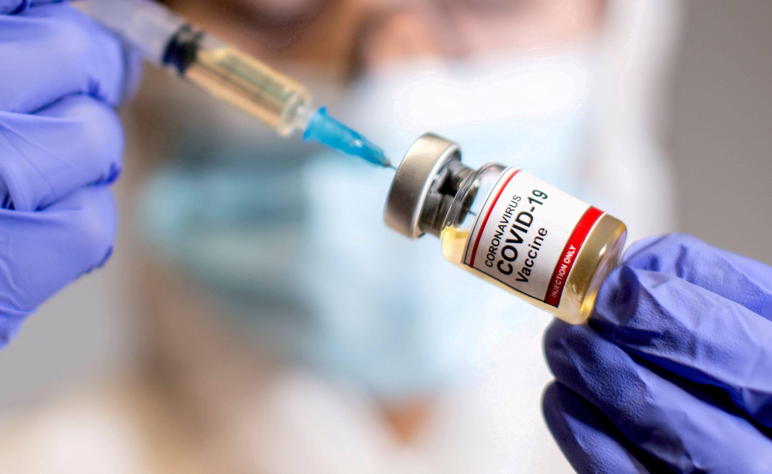 FILE PHOTO: A woman holds a small bottle labelled with a "Coronavirus COVID-19 Vaccine" sticker and a medical syringe in this illustration taken  October 30, 2020. REUTERS/Dado Ruvic