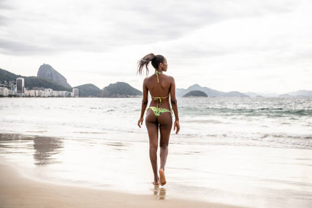 Slim woman walking on sandy beach and looking away towards sea, views of Rio de Janeiro in distance, woman on vacation, solitude, getting away from it all