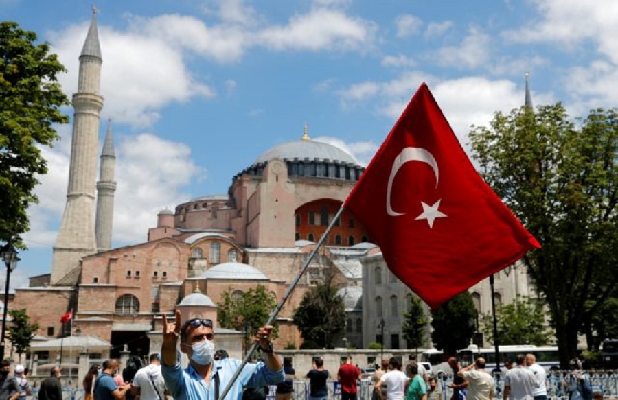 Man waves a Turkish flag as he makes the nationalist grey wolf sign in front of the Hagia Sophia or Ayasofya-i Kebir Camii in Istanbul,