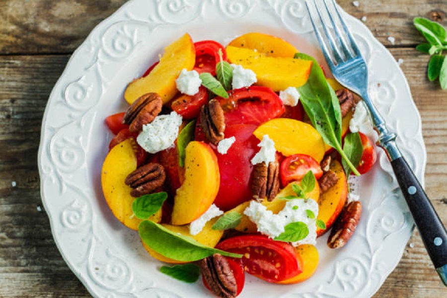 Summer peach tomato salad with basil, baby spinach, feta cheese and pecan nuts. Summer appetizer food. Picnic outdoor concept