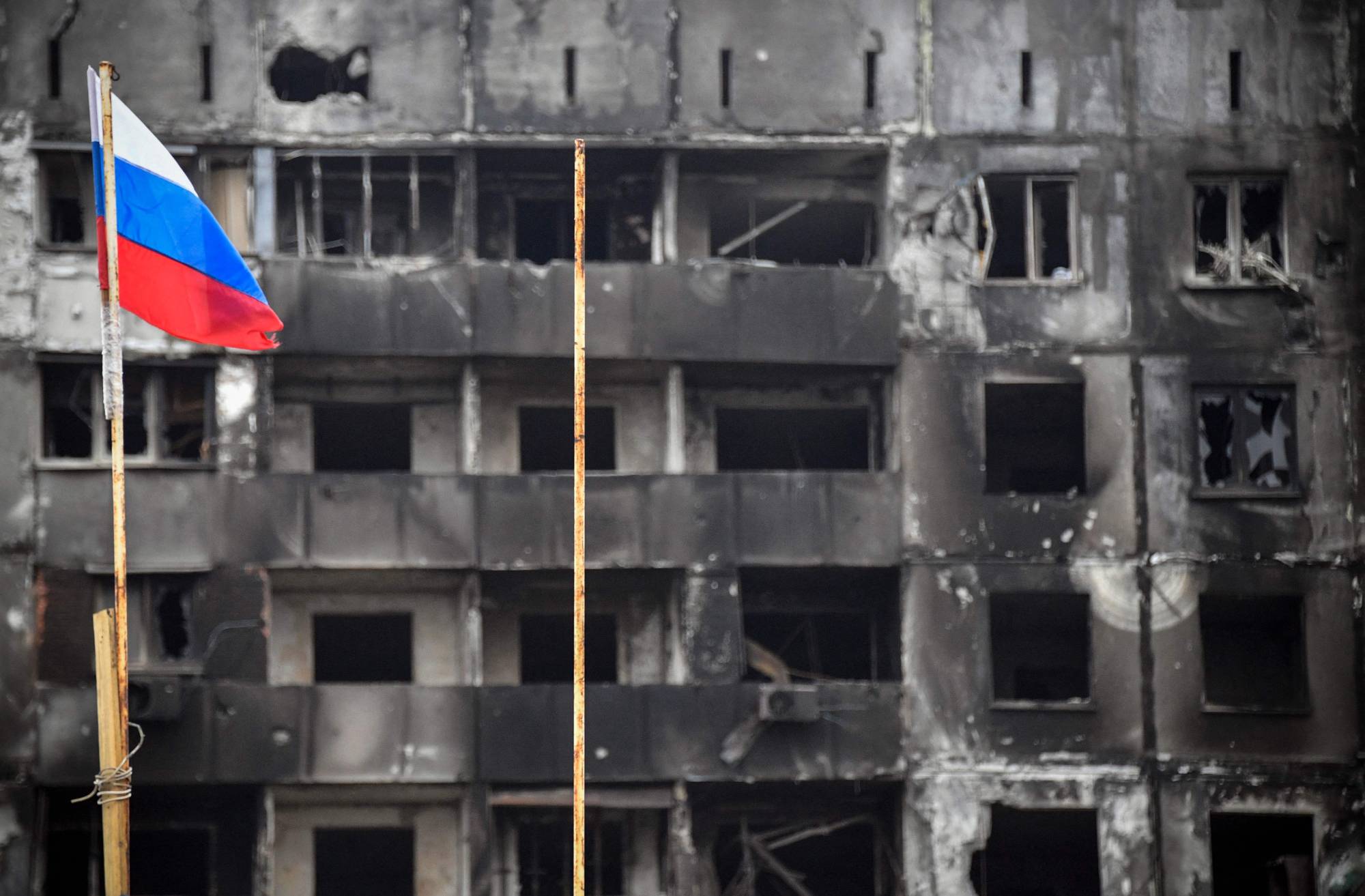 TOPSHOT - A Russian national flag flies by destroyed buildings in Mariupol on April 12, 2022, as Russian troops intensify a campaign to take the strategic port city, part of an anticipated massive onslaught across eastern Ukraine, while Russia's President makes a defiant case for the war on Russia's neighbour. - *EDITOR'S NOTE: This picture was taken during a trip organized by the Russian military.* (Photo by Alexander NEMENOV / AFP)