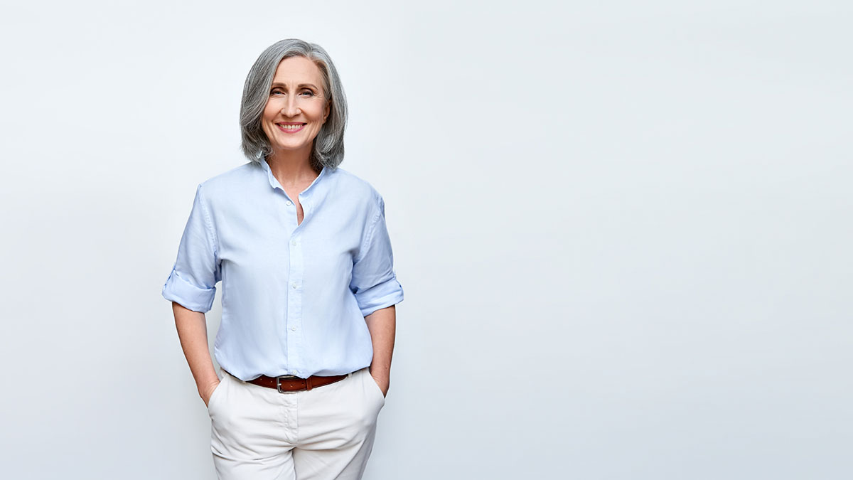 Smiling beautiful mature business woman standing isolated on white background. Older senior businesswoman, 60s grey haired lady professional female ceo, coach looking at camera, banner, copy space.