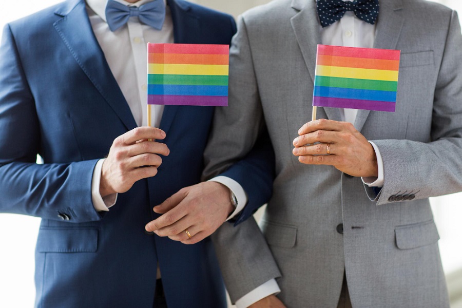 people-homosexuality-same-sex-marriage-love-concept-close-up-happy-male-gay-couple-suits-bow-ties-with-wedding-rings-holding-rainbow-flags