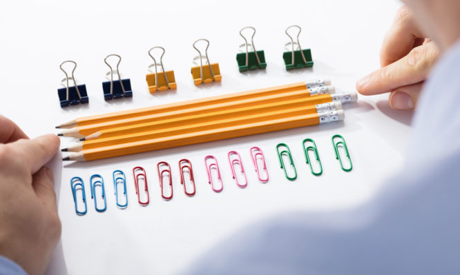 Businessman Arranging The Pencils In Between The Row Of Colorful Pins And Paper Clips